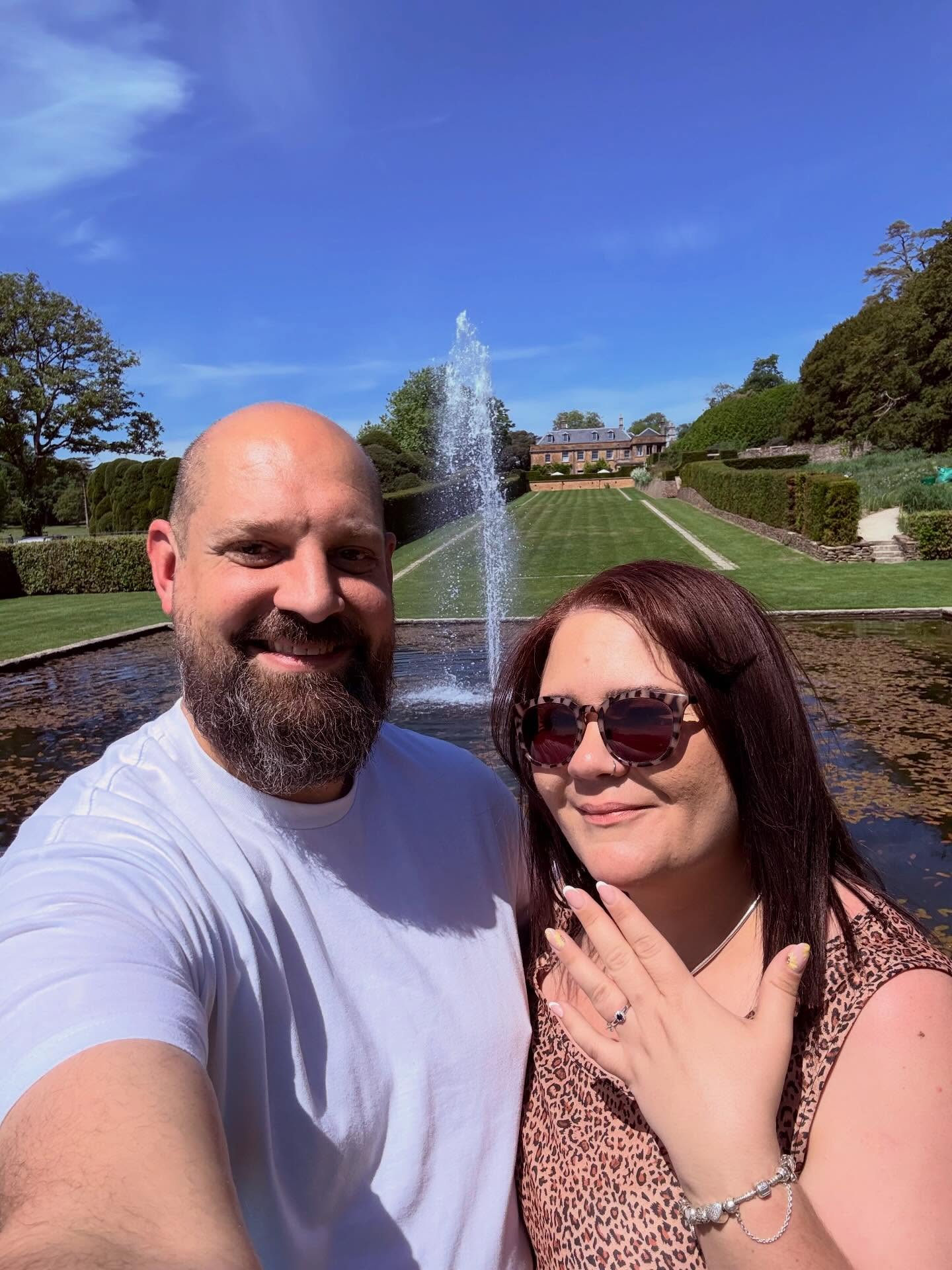 Robert and Lucy showing off the engagement ring by the fountain